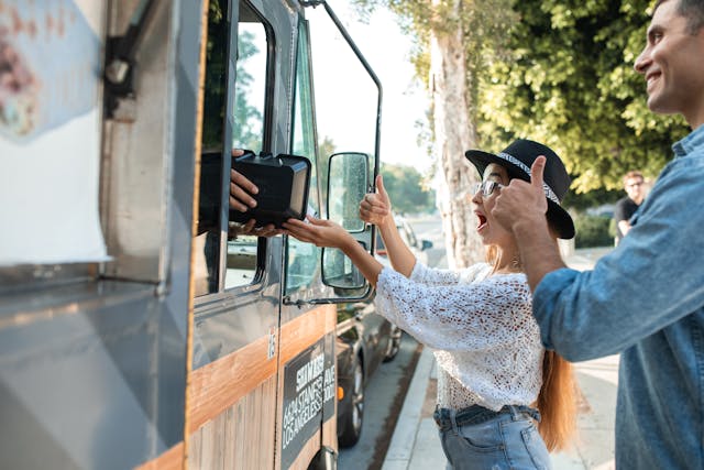 Two people standing in front of a food truck, excited about their purchase
