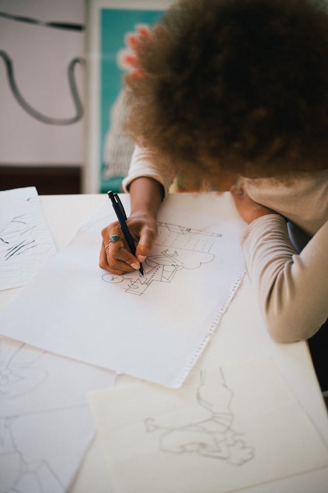 A concept artist creating sketches on white pieces of paper at their desk. 
