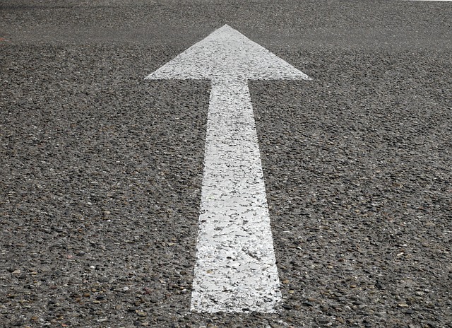 A close-up of a white arrow on a road pointing forward, representing the right path. 
