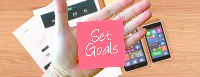 A close-up of a hand holding a pink sticky note that reads the phrase, “Set Goals.”
