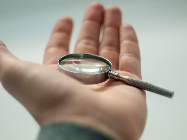 A close-up of a person’s open hand holding a small magnifying glass. 