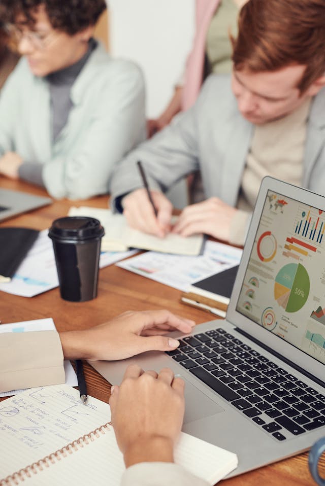 A person uses a laptop full of pie charts and graphs during a meeting with other analysts. 
