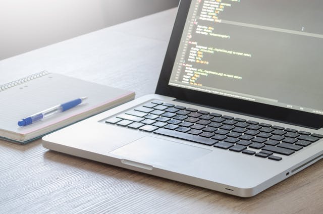 A close-up of a laptop displaying lines of code next to an open notebook.
