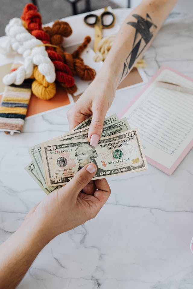Two people exchange several US dollar banknotes over a white marble table. 
