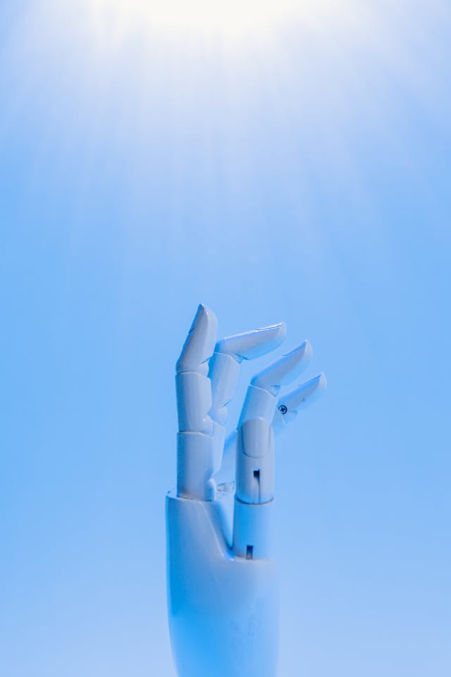 A white robotic hand points upward against a bright blue background. 
