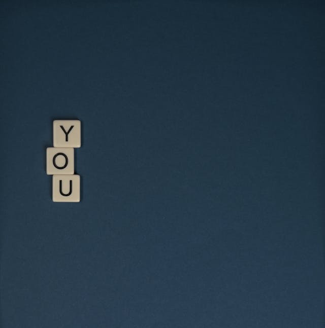 A bird’s-eye view of three Scrabble tiles that spell out the word “You” against a dark blue background.