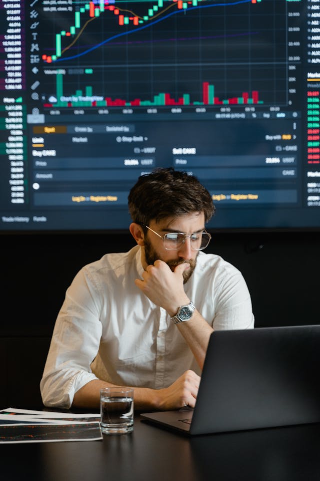 A man works on his laptop in front of a board that is full of data visualizations. 