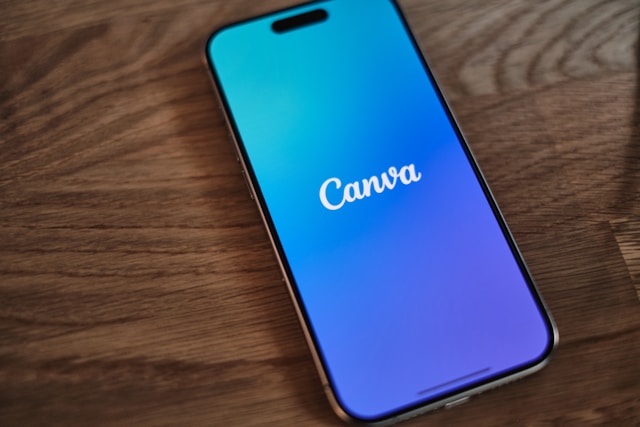 A cell phone with the Canva app open sitting on top of a wooden table.