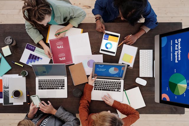 A picture of a group of people sitting at a table surrounded by books and laptops.
